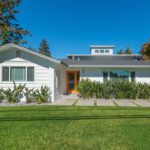 A white house surrounded by green grass and trees under a clear blue sky.