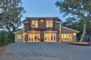 image of the front of a home made of large stone and many large white windows.