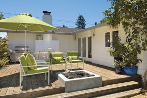 Wooden outdoor deck furnished with green chairs, umbrella, and grill