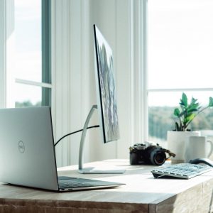 Laptop and monitors placed on a desk in a home next to a large window