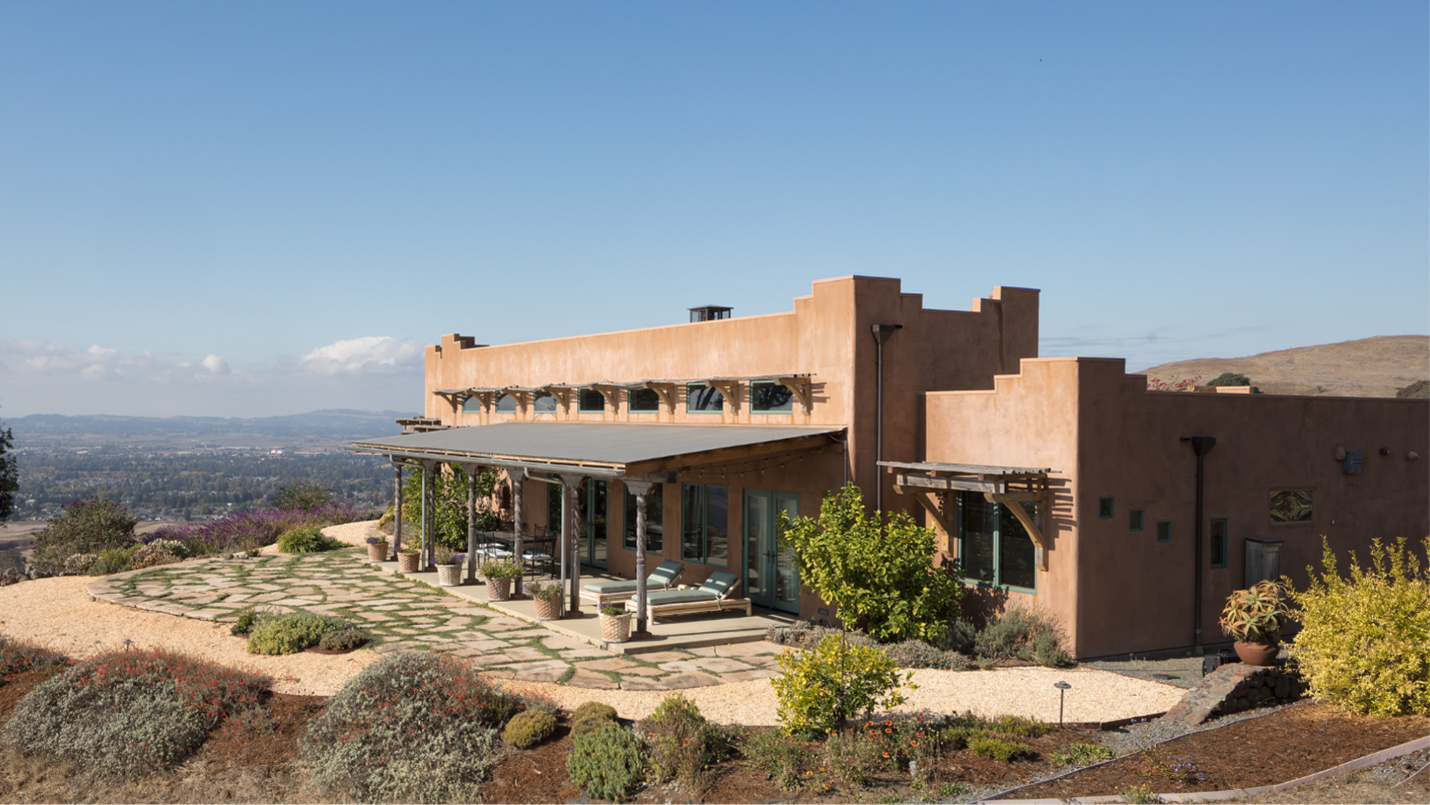 A house with a beautiful covered outdoor space sits on a hill overlooking a town.