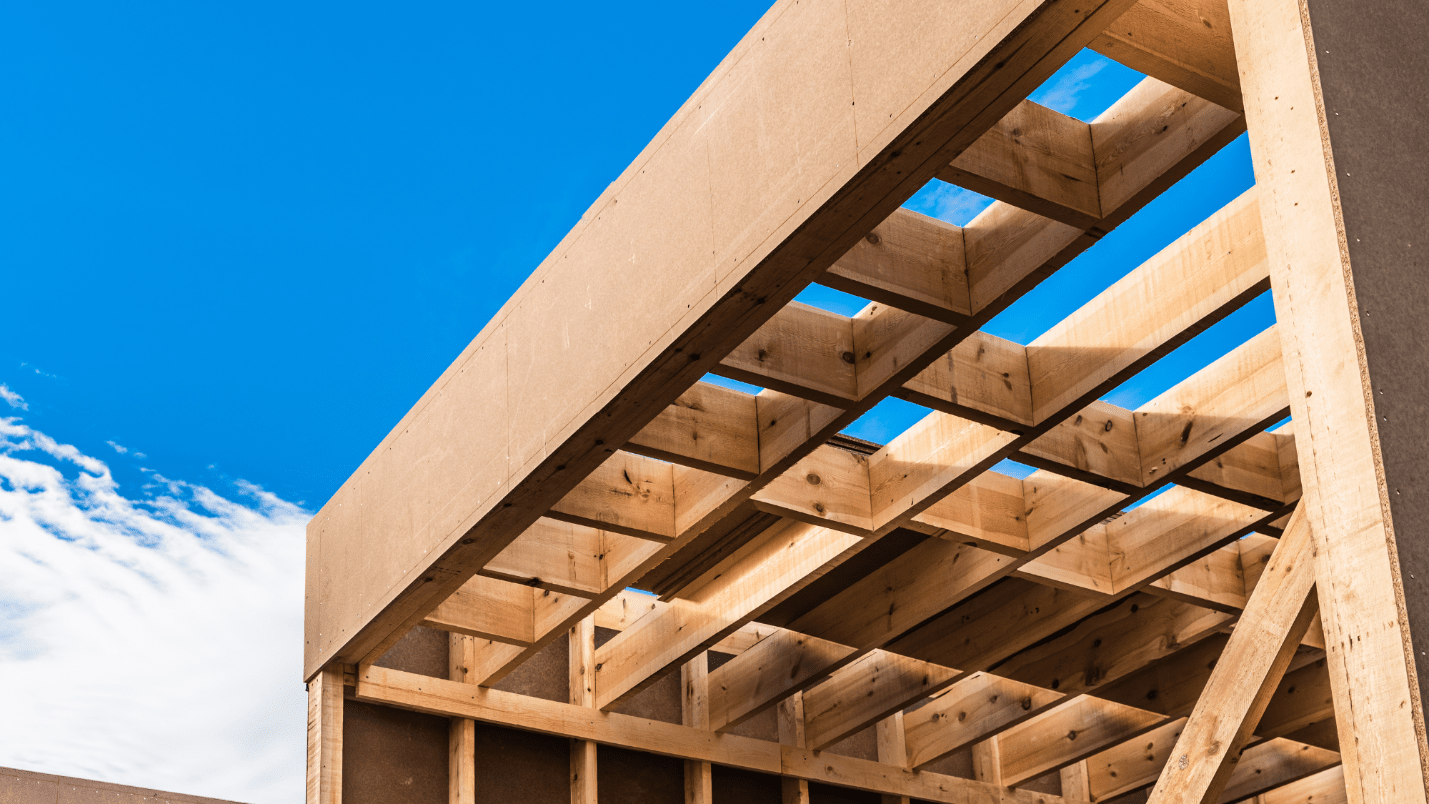 A house frame is being constructed and behind it, there is a blue sky.