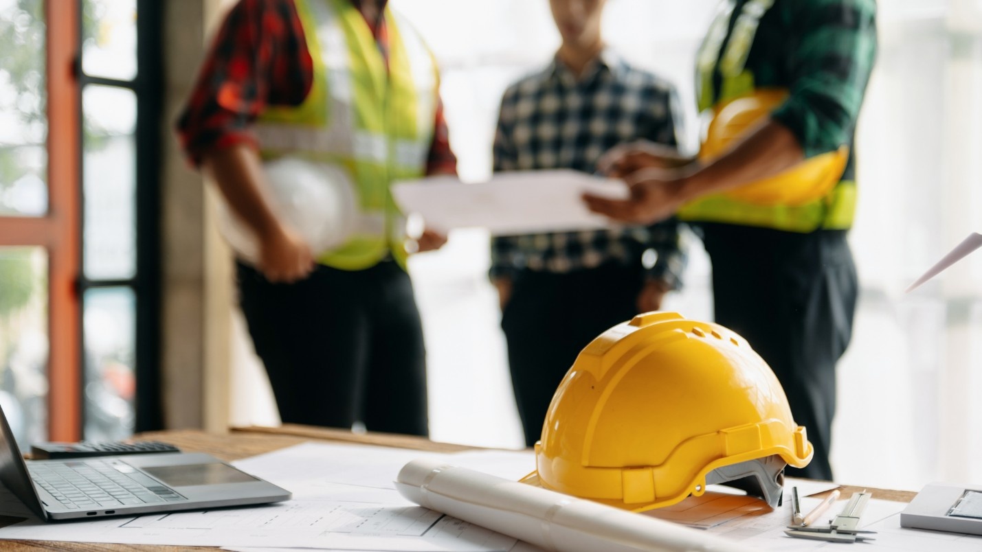 Three workers in hardhats and high-visibility gear look at a blueprint.