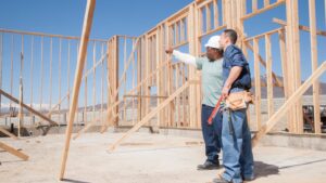 Two home builders examine the frame of a house in progress.