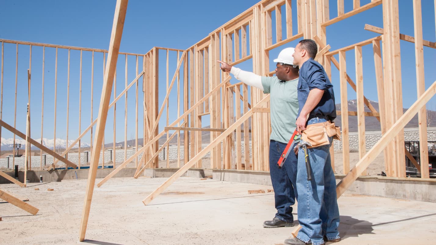 Two home builders examine the frame of a house in progress.