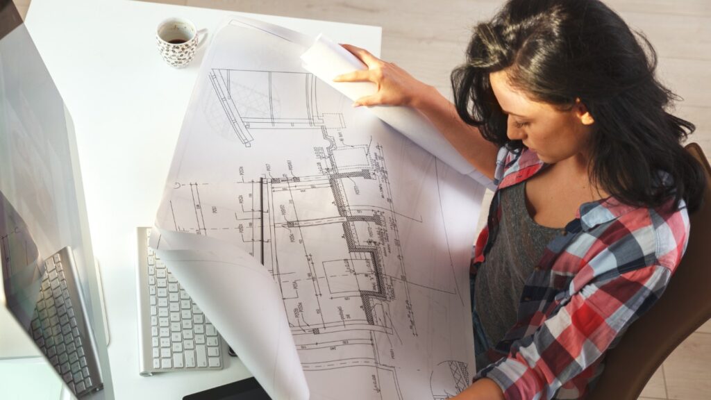 A female architect reviews the latest draft of a construction blueprint.