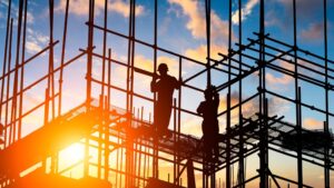 Two construction workers stand on scaffolding at sunset.