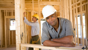 A contractor leans on the framing of their home project and smiles.
